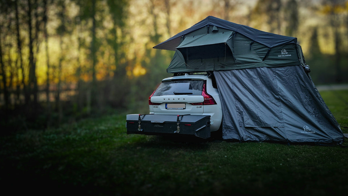 Voiture équipée d'un IXTAbox sur la boule d'attelage et d'une tente de toit, chargée pour un voyage en famille